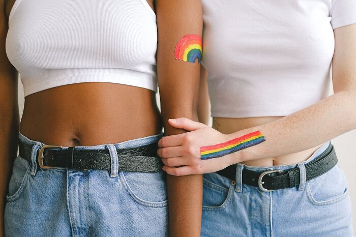 Two young people wearing white tops and jeans with rainbow pride tattoos on their arms showing support for Gen Z.