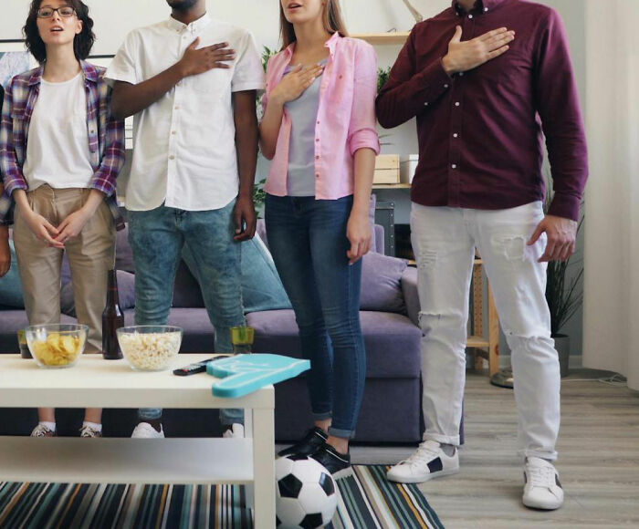 Friends standing with hands over hearts, embodying pinnacle dad humor in a living room setting.