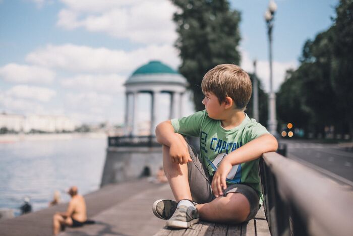 Young boy sitting alone by the waterfront, looking away, capturing a moment from a vacation with frightening stories.