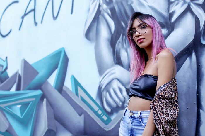 Young woman with pink hair posing by graffiti wall, representing Gen Z style admired by people in their 40s, 50s, and 60s.