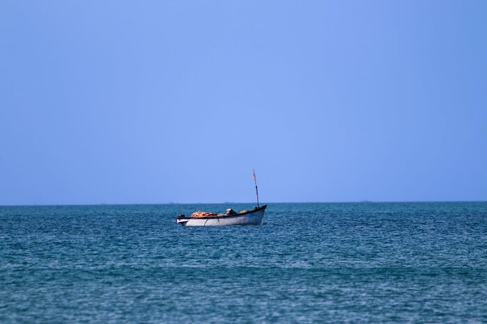 Small fishing boat floating alone on calm sea under clear blue sky, hinting at unexpected frightening vacation stories.