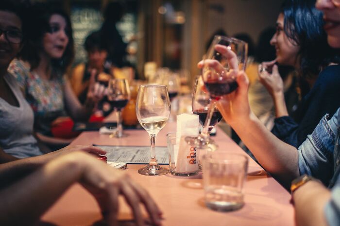 Group of friends at a restaurant table holding glasses of wine, sharing stories instead of a relaxing vacation.