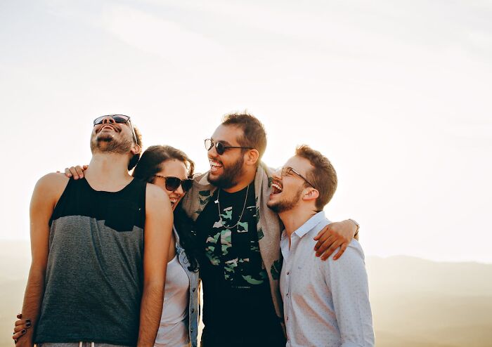 A group of four joyful people in their 40s to 60s wearing sunglasses, enjoying time together outdoors at sunset.
