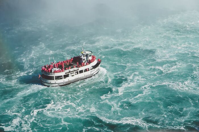 Boat filled with tourists in red raincoats facing rough, swirling waters, capturing frightening vacation stories.