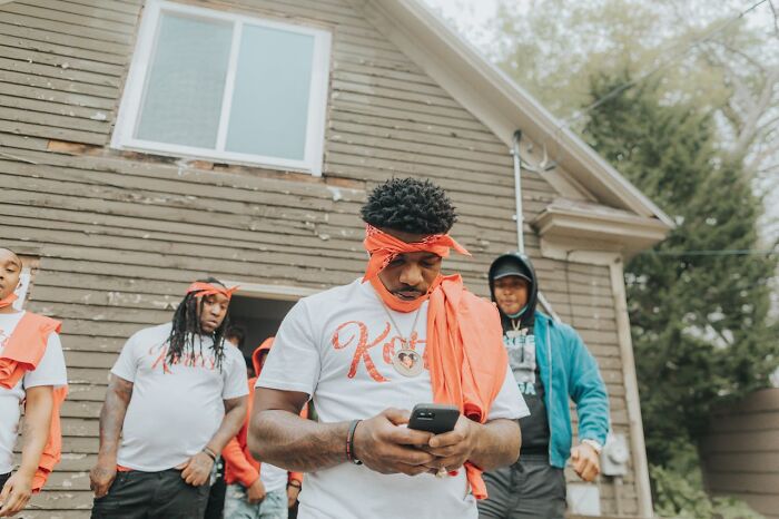 Group of young men outside a house, one focused on phone, representing people left with frightening vacation stories.