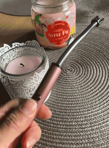 Hand holding an electric candle lighter near a lit scented candle, showcasing one of the year's amazing discoveries.
