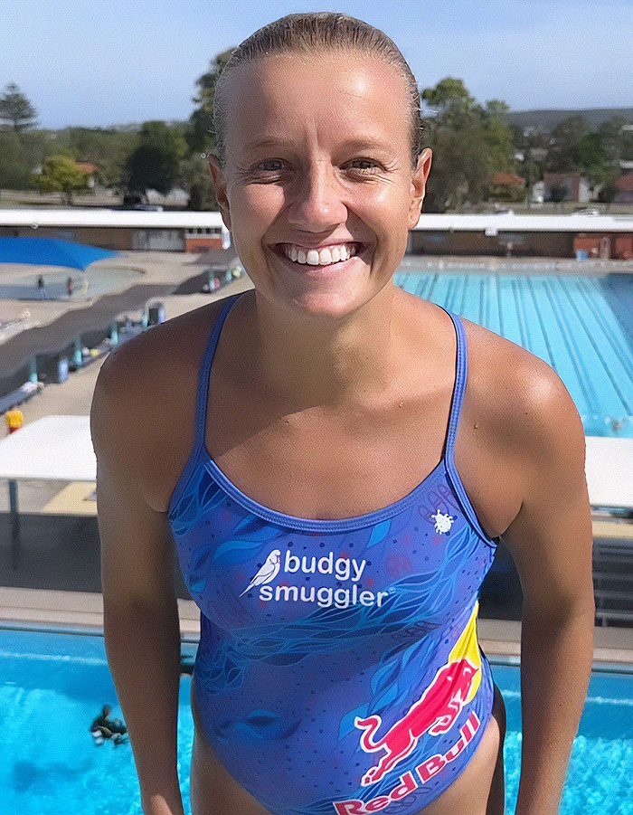 Female thrill-seeking diver in swimsuit smiling at poolside before extreme waterslide jump.
