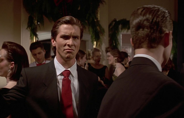 "Christian Bale in American Psycho, displaying the iconic Sigma Face expression at a formal party.