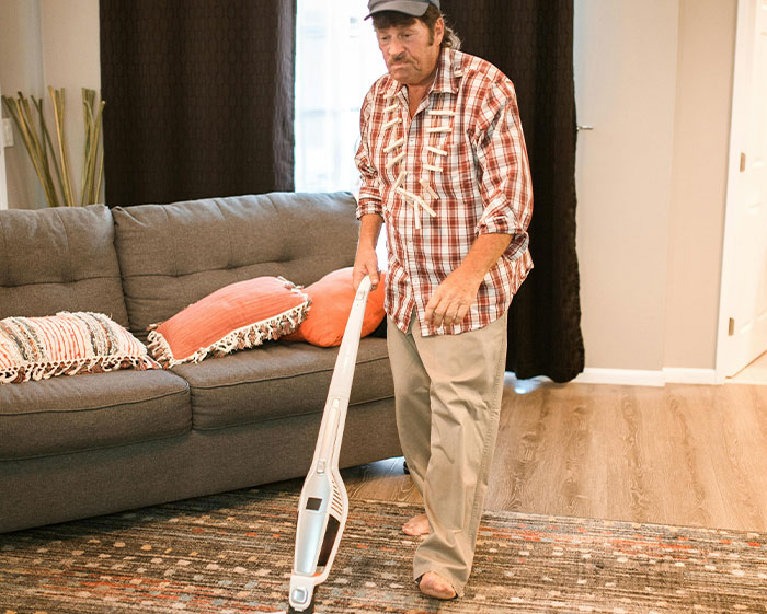 Man in a plaid shirt vacuuming carpet in a living room, illustrating strict house rules that left guests grimacing.