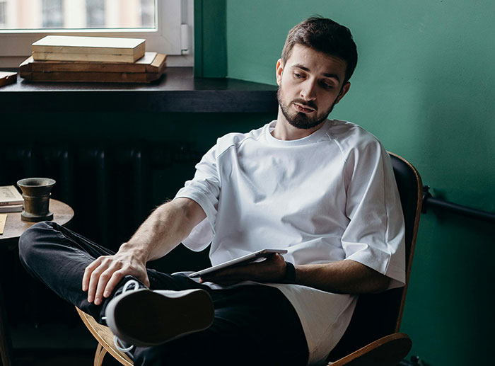 Man in white shirt sitting thoughtfully in chair, reflecting on unusual house rules that left guests grimacing.