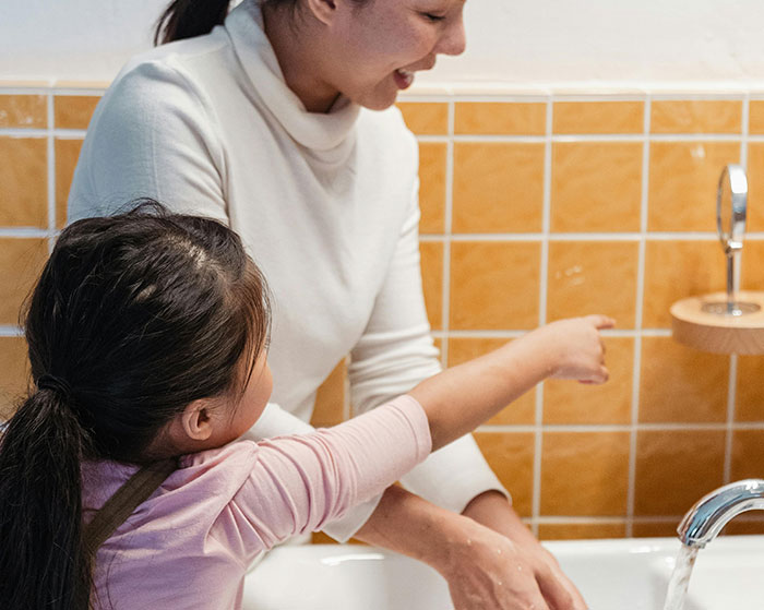 Mother and daughter washing hands together in a bathroom, illustrating family house rules that surprise guests.