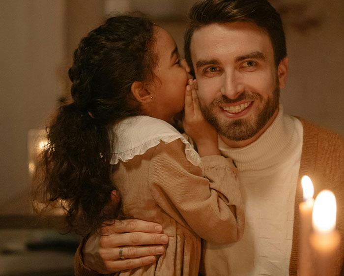 Man smiling while a young girl whispers in his ear, illustrating house rules that left guests grimacing.