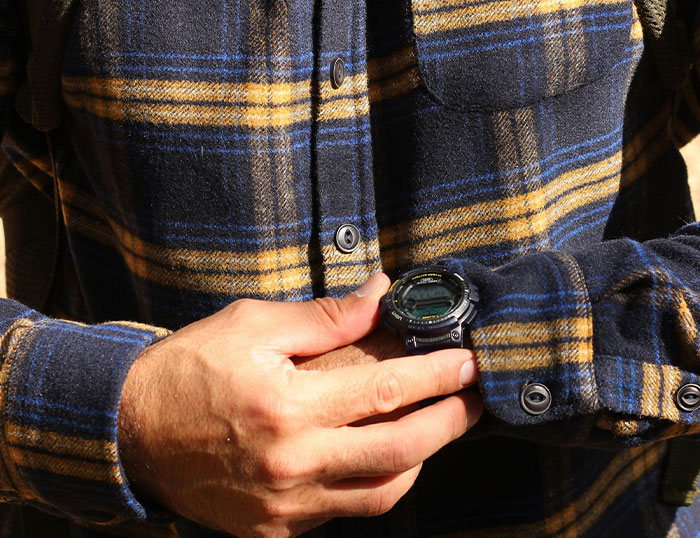 Man wearing a yellow and blue plaid shirt adjusting a black digital wristwatch, reflecting house rules that left guests grimacing.