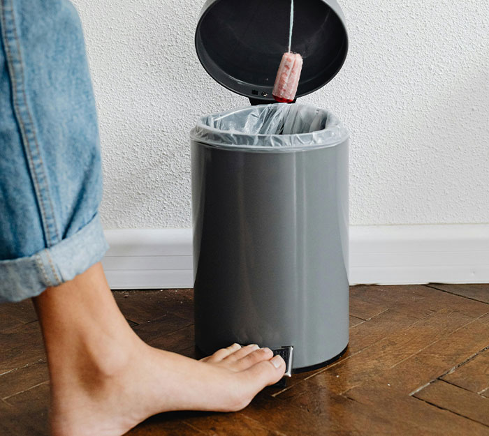 Person wearing jeans using foot pedal to open a trash can in a house with strict house rules