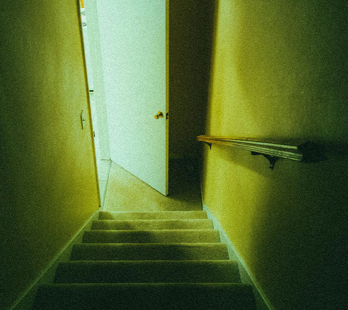 Dimly lit staircase leading to an open door in a house, illustrating the mood of unusual house rules and guest discomfort.