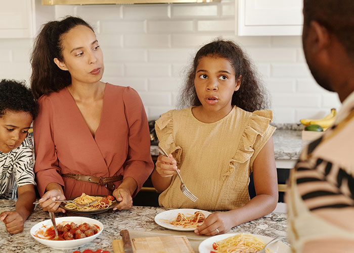 Family having a tense conversation during dinner in kitchen, reflecting strict house rules that left guests grimacing.