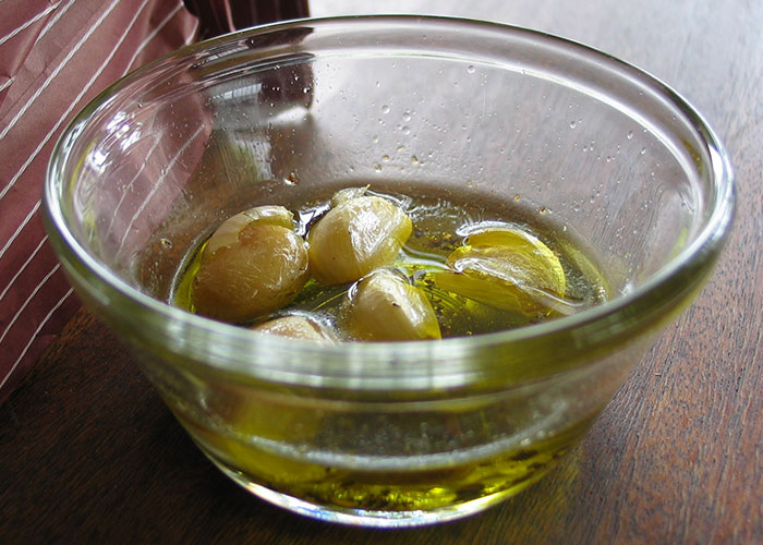 Glass bowl with garlic cloves soaking in oil on a wooden table, highlighting everyday things that can be deadly.