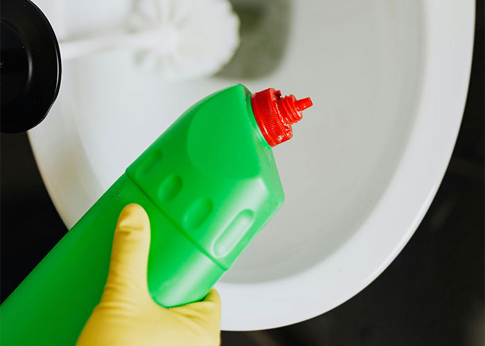 Hand in yellow glove holding green cleaning bottle over toilet bowl illustrating deadly everyday things risk.