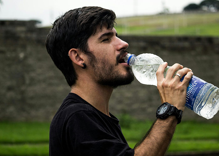 Man drinking water from plastic bottle outdoors, highlighting everyday things most people don’t realize are deadly.