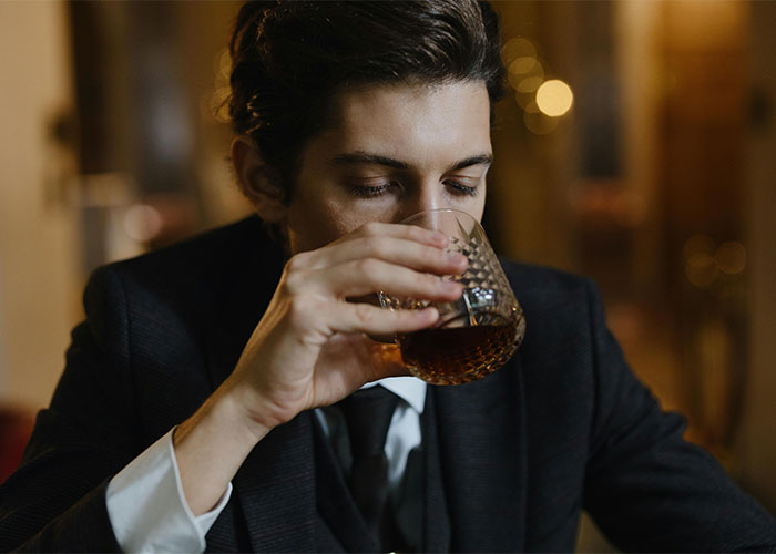 Young man in a suit drinking alcohol indoors, illustrating everyday things most people don’t realize are deadly.
