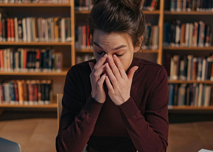 Young woman stressed and tired rubbing eyes in a library, highlighting the deadly risks of everyday things.