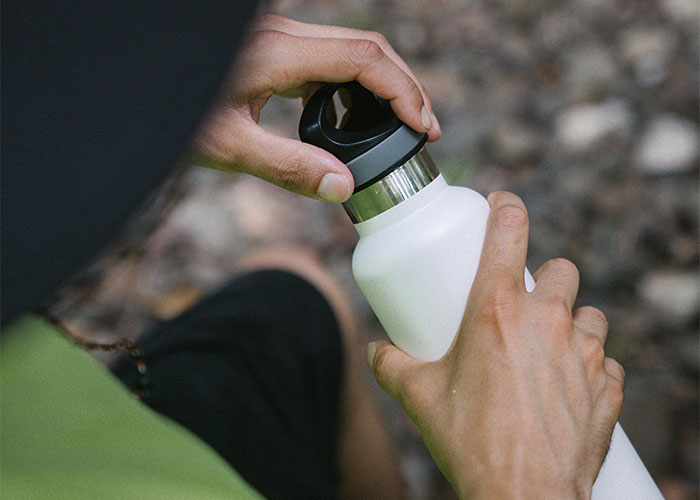 Person holding and opening a white water bottle outdoors highlighting deadly everyday items awareness.