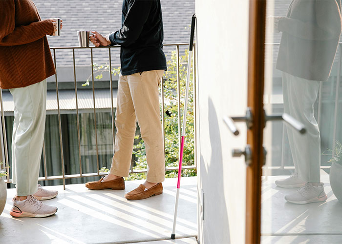 Two people standing and talking on a balcony next to a white cane, highlighting everyday things most people don’t realize are deadly.