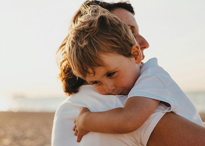 Young child hugging parent on the beach at sunset, capturing moments of parenting and family connection.