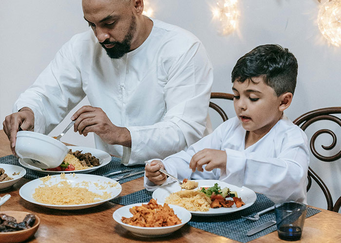 Father and son in traditional clothing sharing a meal at the table, capturing moments of parenting and family bonding.