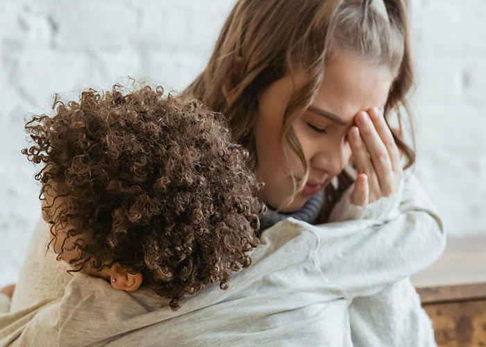 Stressed mother covering face while hugging child, representing emotions linked to feeling like a bad parent.