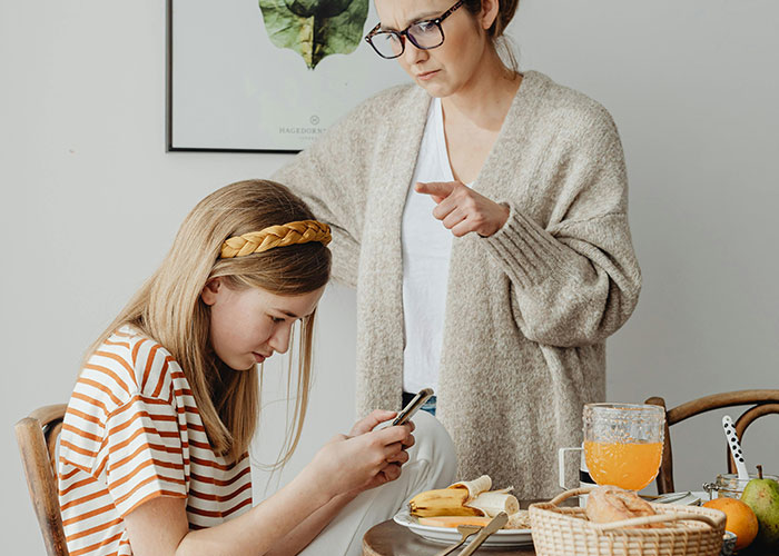 Mother scolding daughter distracted by phone at breakfast, illustrating signs of bad parenting behaviors in a home setting.