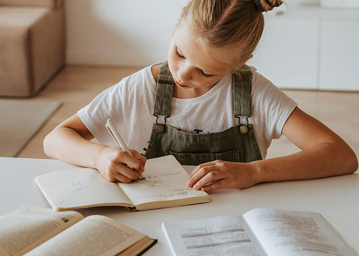 Young girl focused on homework at a table with books, illustrating challenges that might make parents feel like bad parents.