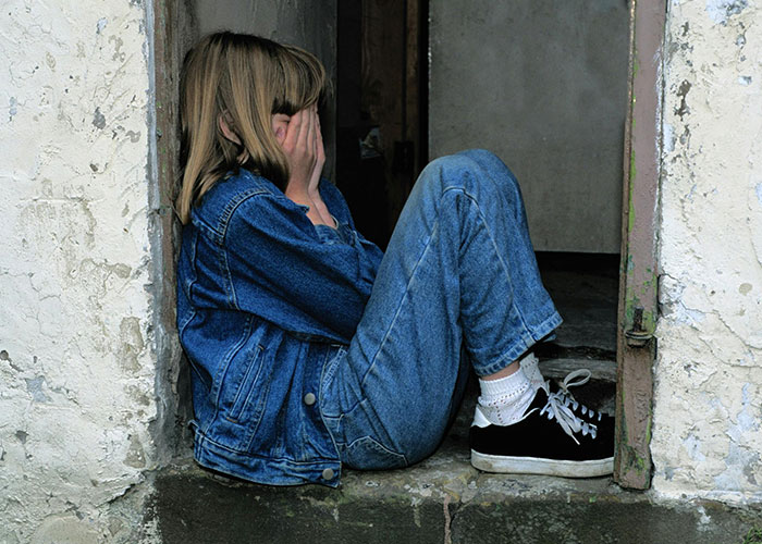 Child sitting alone covering face, portraying emotions often linked to bad parenting concerns and struggles.