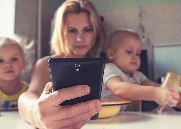Mother distracted by phone while children play nearby, illustrating challenges of bad parenting concerns.