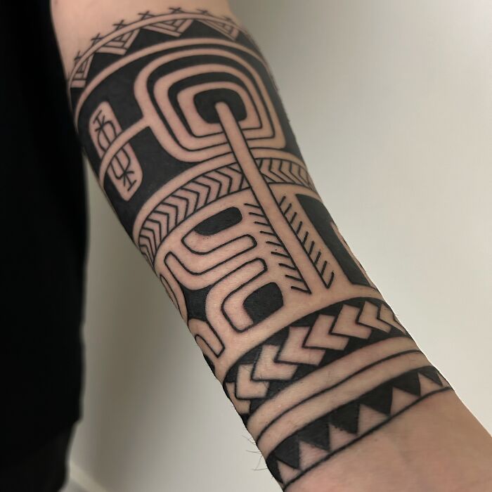 Intricate geometric tattoo on forearm, showcasing bold black lines with complex patterns.