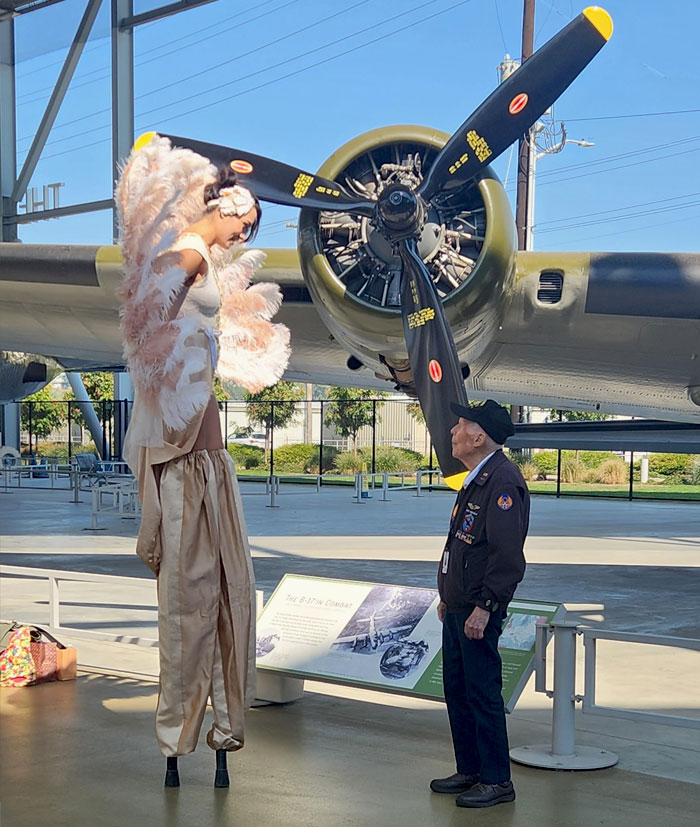 A 100-Year-Old WWII Vet Admires A Stilt-Walking Performance Artist