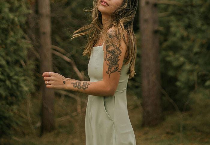 Woman with dark tattoo sleeves in a green dress, standing outdoors.