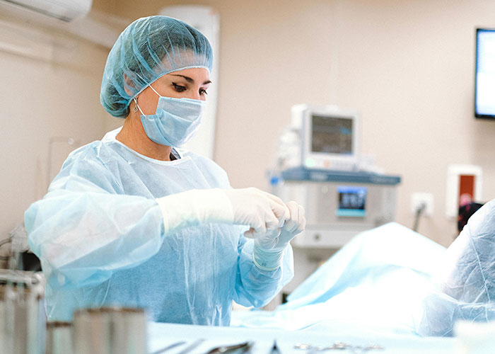 Woman in medical scrubs and mask preparing gloves in a sterile environment, symbolizing the traditional wives work is never done theme.