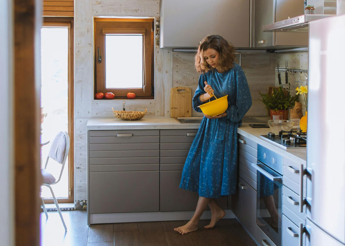 Woman in a blue dress mixing ingredients in a kitchen, illustrating traditional wives’ daily household work experiences.