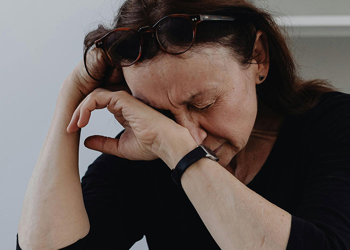 Middle-aged woman with glasses on head resting her face on hand, reflecting the struggles of traditional wives.