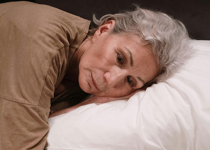 Older woman with gray hair lying on a pillow, reflecting on traditional wives experiences from the 20th century.