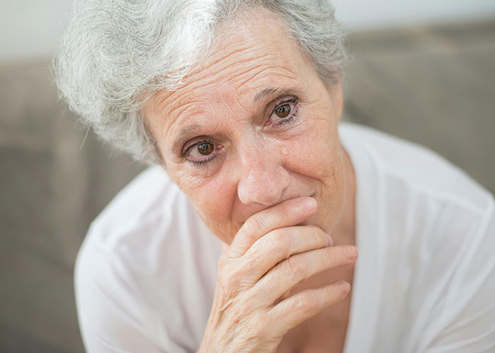 Elderly woman with gray hair and teary eyes reflecting on traditional wives 20th century real experiences