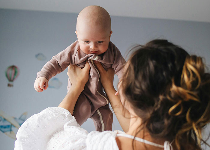 Mother lifting her baby in a nursery, illustrating traditional wives from the 20th century real experiences.