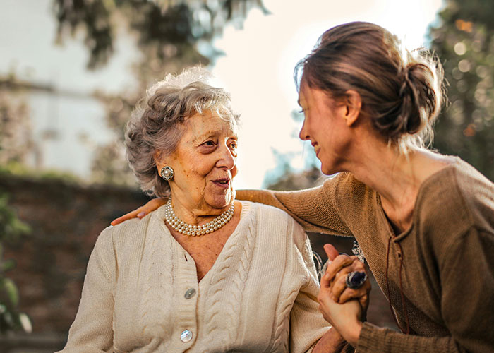 Elderly traditional wife and younger woman sharing a heartfelt moment outdoors, reflecting real experiences from the 20th century.