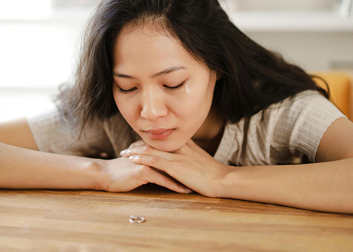 Young woman with tear on cheek resting head on folded arms, reflecting on traditional wives' real experiences.