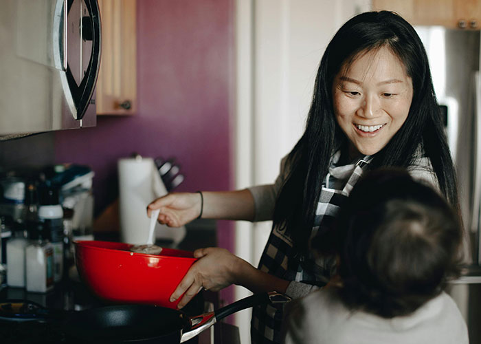 Woman smiling while cooking in a kitchen, demonstrating traditional wives’ daily domestic work and multitasking.