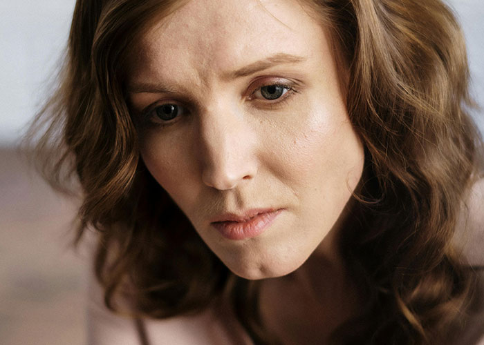Woman with wavy hair looking down thoughtfully, depicting the emotional toll of traditional wives' daily work.