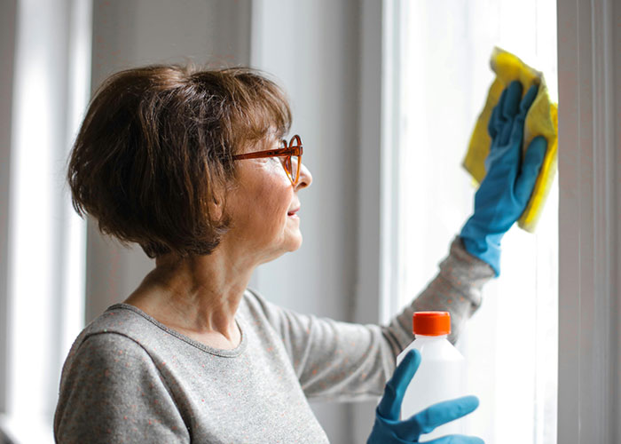 Middle-aged traditional wife cleaning a window wearing gloves and eyeglasses, reflecting 20th century home experiences.