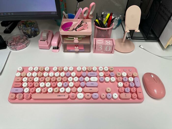 Pink retro-style keyboard and mouse on a desk surrounded by cute pink office supplies in weirdly wonderful finds collection.