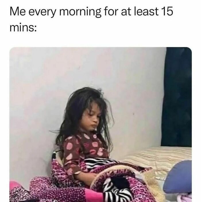 A tired-looking child in pajamas sits on a bed, resembling funny memes about mornings.